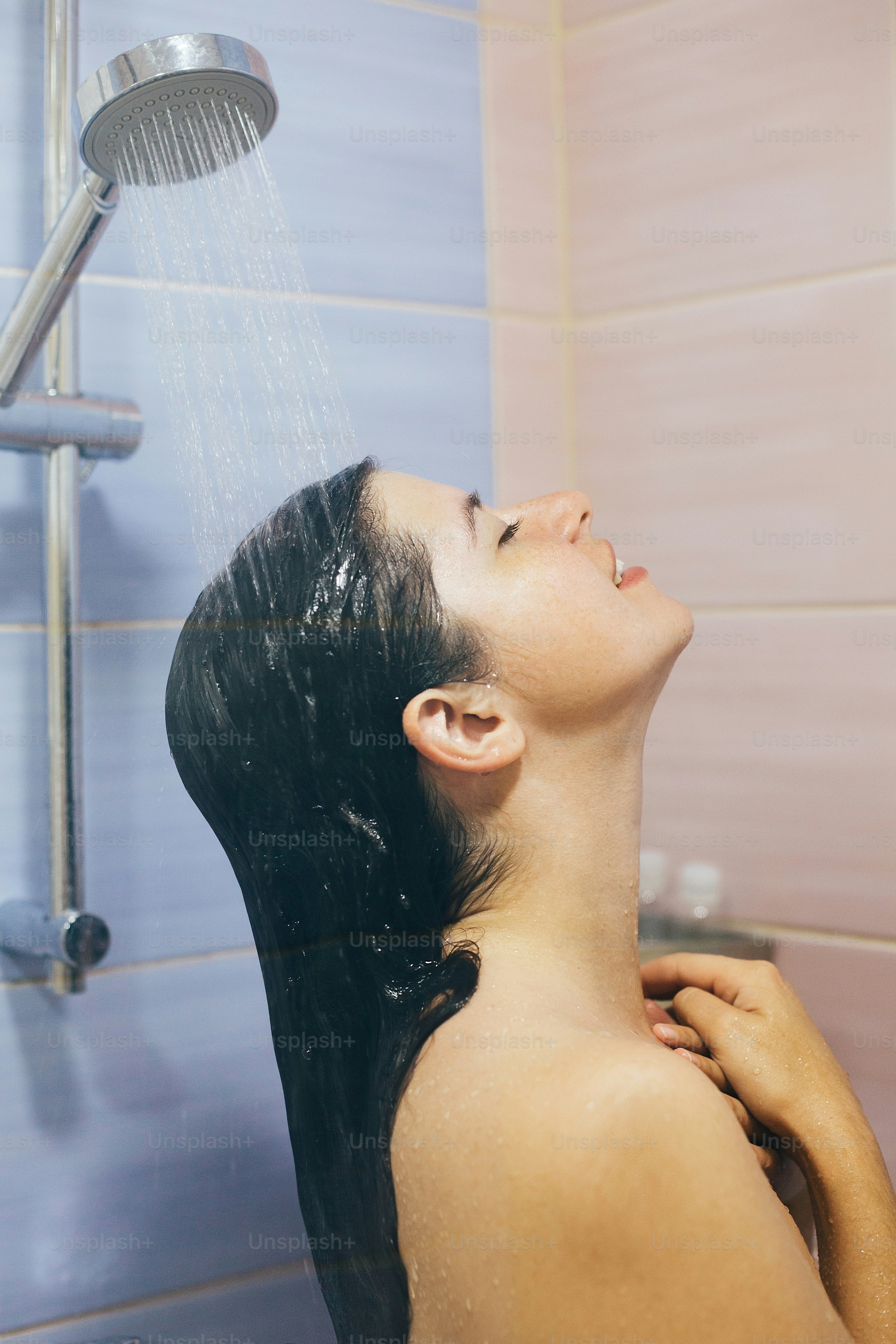 Young happy woman taking hot shower at home or hotel bathroom. Beautiful brunette girl washing her hair and enjoying relax time. Body and skin hygiene, lifestyle concept
